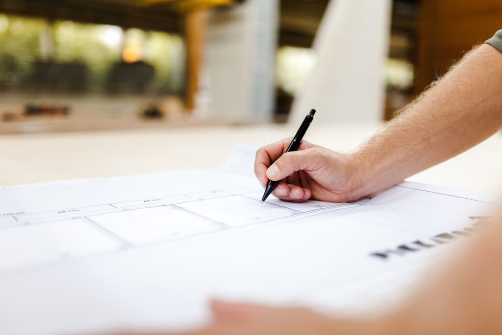 Close-up of an appraiser's hands using a scale ruler and calculator to analyze architectural blueprints on a clean, modern...