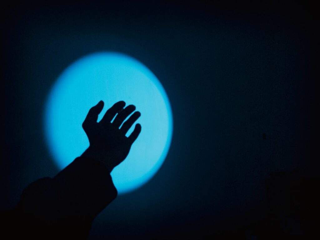 Close-up of a human hand gently touching an abstract, glowing orb of blue and purple light in a dark, modern setting, symb...