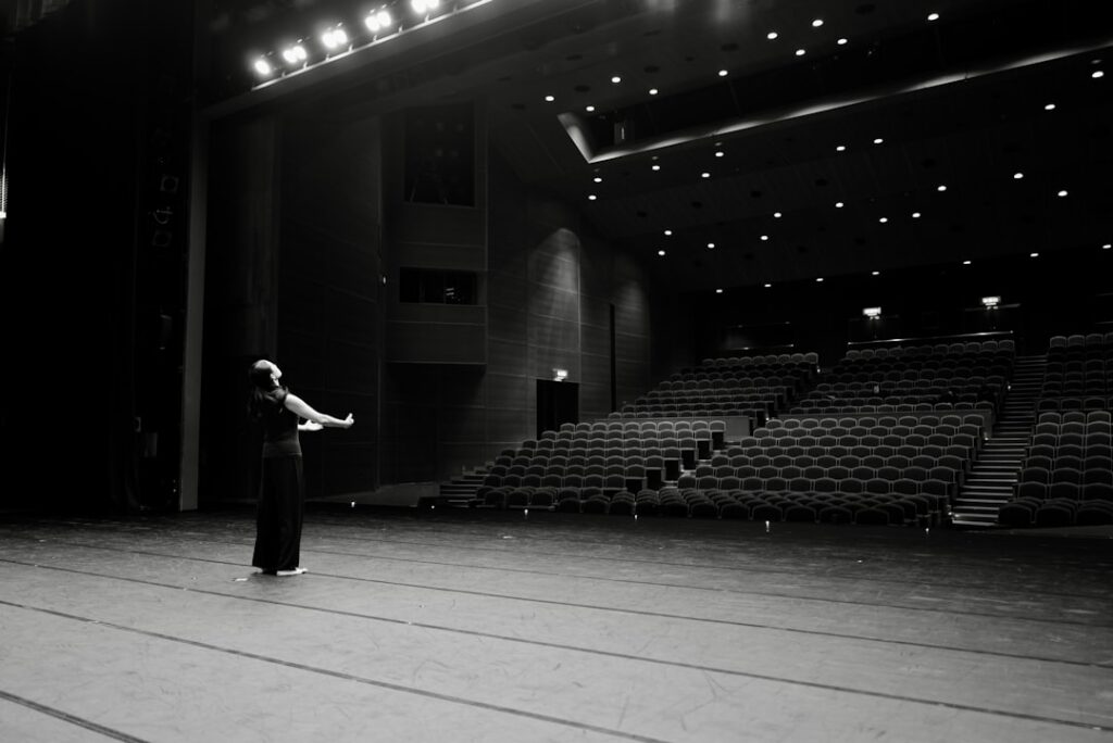 Conductor seen from behind, arms outstretched, leading a symphony orchestra under dramatic stage lighting, symbolizing con...