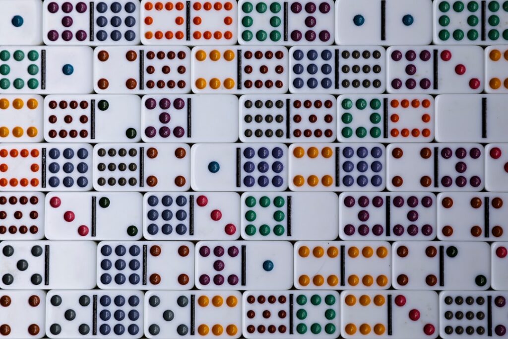 Close-up of a line of dark dominoes falling in a cascading chain reaction on a clean, minimal background, symbolizing the ...