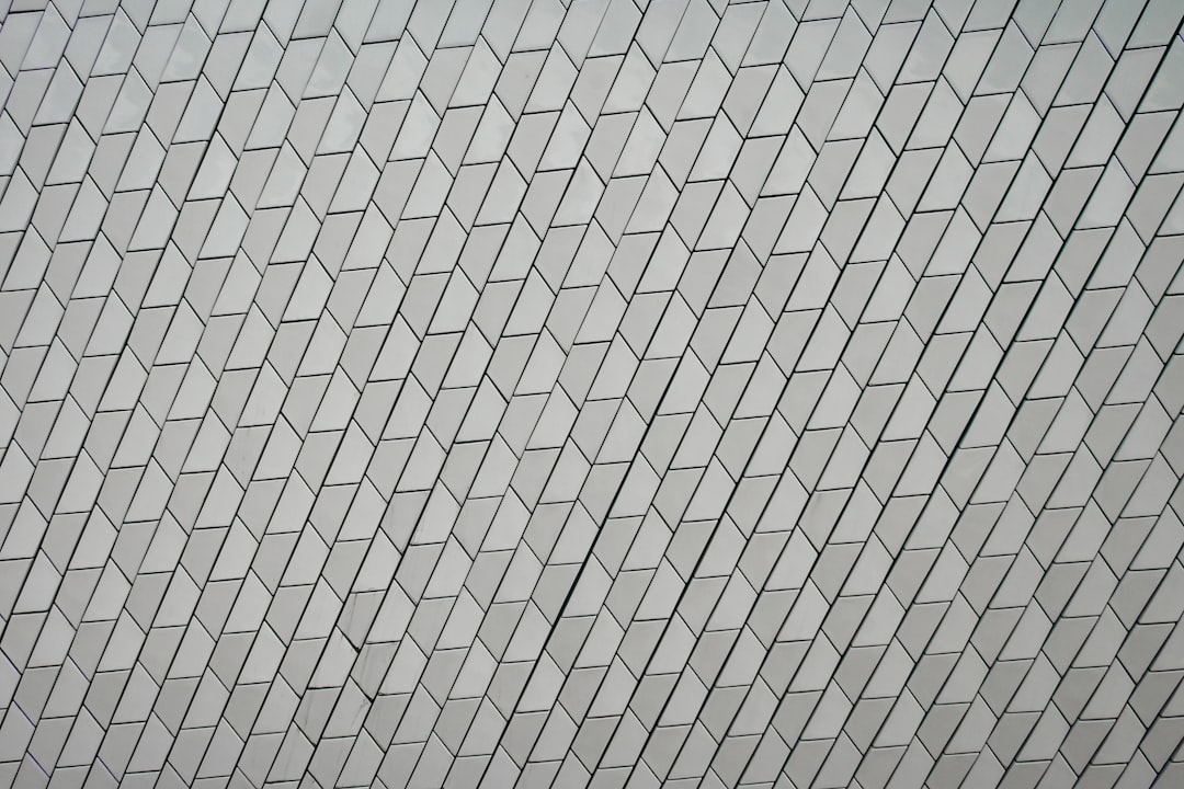 A single person walking across and disrupting a vast, clean, repeating geometric pattern on the ground, illustrating a leader forging a new path.
