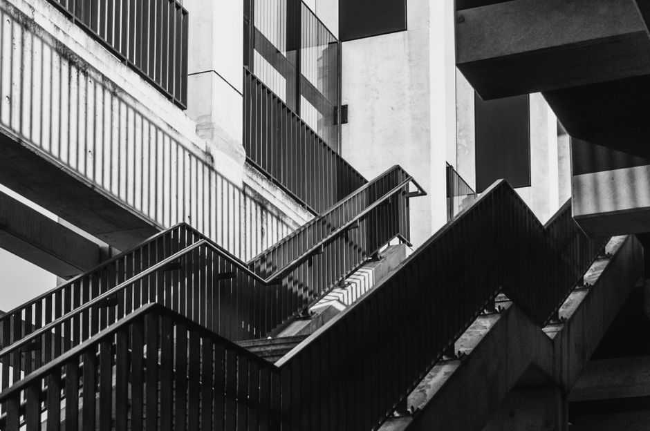 A bright, modern photograph of an abstract concrete staircase leading in a confusing, impossible direction, illustrating the paradox of AI-induced innovation lag where activity doesn't equal progress.